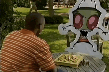 a man is sitting at a table playing chess with a cardboard cutout of a monster .