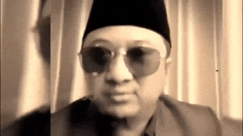 a man wearing sunglasses and a hat is sitting in front of a window .