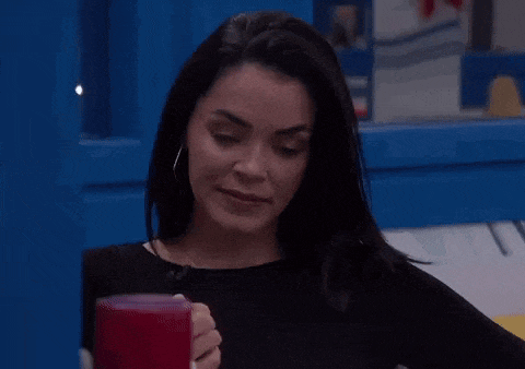 a woman is sitting at a table holding a red cup and looking at the camera .