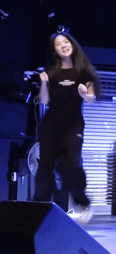 a woman in a black shirt is jumping in the air on a stage