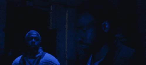 two men are standing in a dark room with a blue light shining on them
