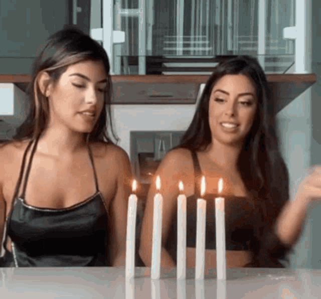 two women are sitting at a table with candles lit up