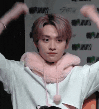 a young man wearing a pink scarf around his neck holds his hands up in the air