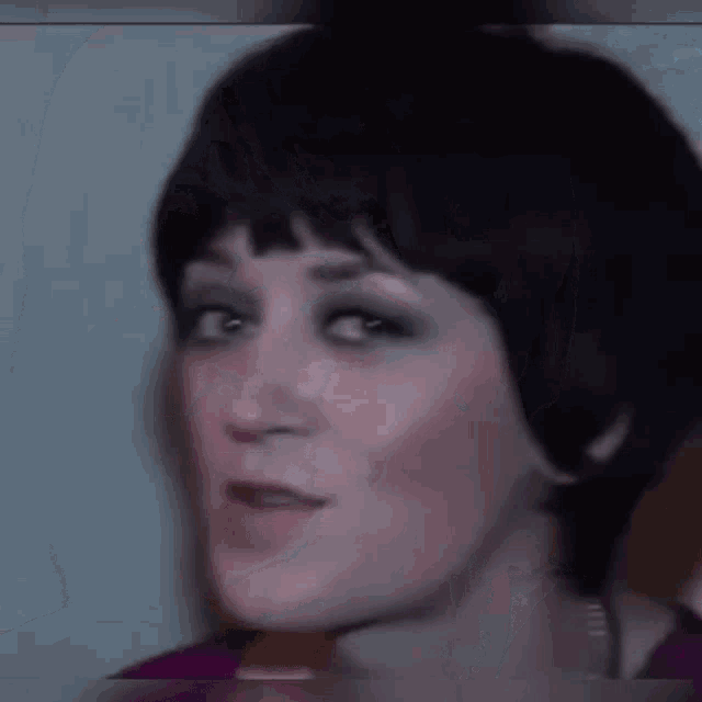 a close up of a woman 's face with short black hair and a purple top .