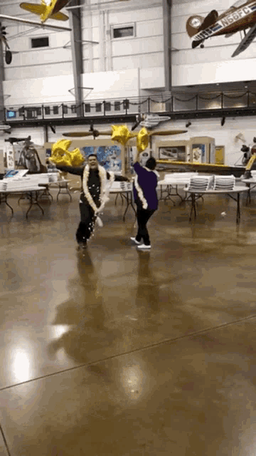 two people holding balloons in a room with planes hanging from the ceiling including one that says n358pe