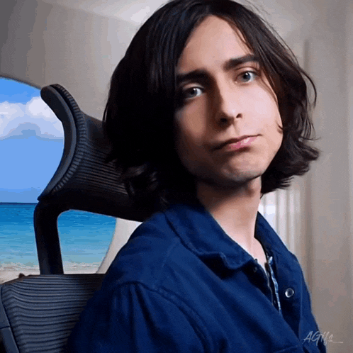 a young man with long hair is sitting in a chair