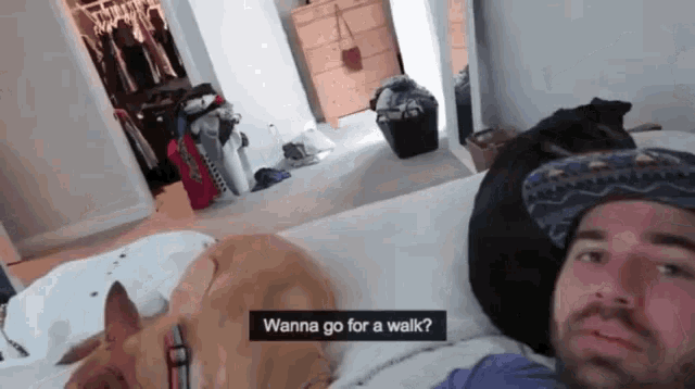 a man laying on a bed with a dog asking if he wants to go for a walk