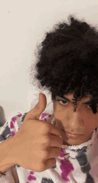 a young man with curly hair gives a thumbs up