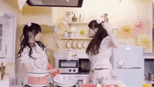 two girls are cooking in a kitchen and one of them is holding a pan .