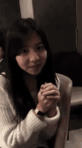 a woman in a white sweater is sitting in a chair with her hands folded
