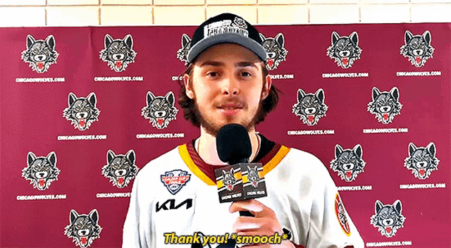 a man in a chicago wolves jersey holds a microphone in front of a wall with wolves on it
