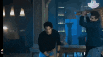 two men are standing next to each other in a room with a table and a lamp .
