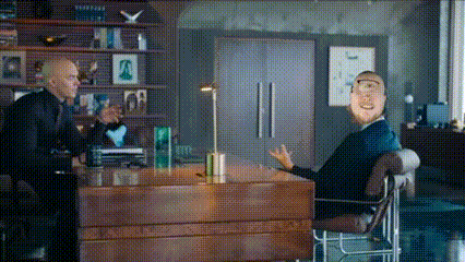 a man in a suit is sitting at a desk talking to another man in a chair .