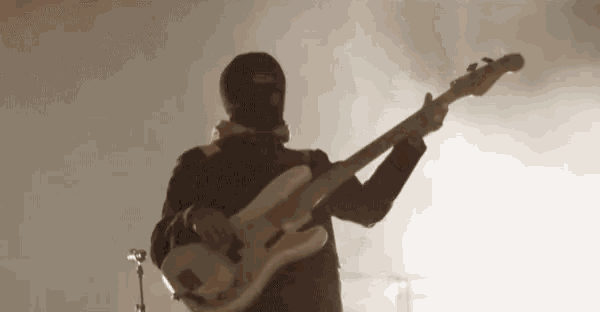 a man wearing a ski mask is playing a bass guitar on stage .