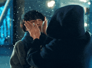 a woman in a hood is touching a man 's face in the rain