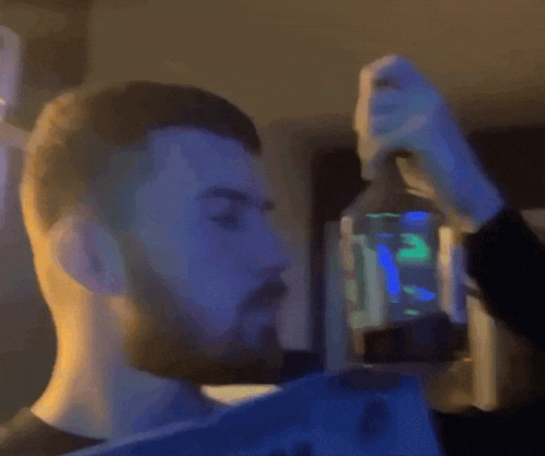 a man with a beard is drinking from a glass bottle