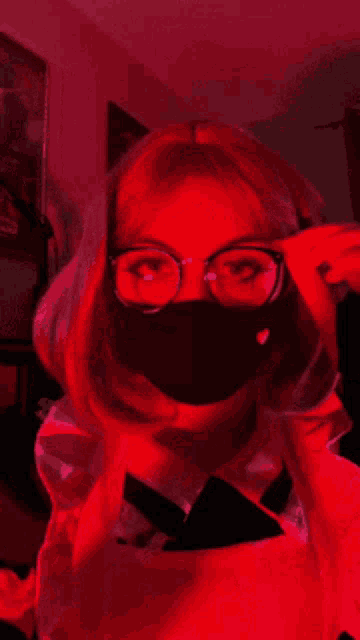 a woman wearing a mask and glasses is standing in a room with red lights .