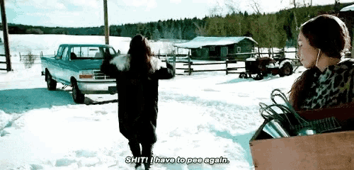 two women are standing in the snow with a truck in the background .