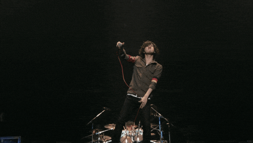 a man singing into a microphone on a stage with a drum set in the background