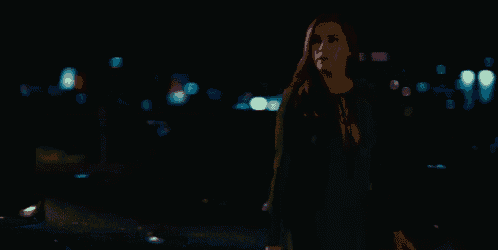 a woman in a green dress is walking down a street at night