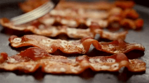 bacon is being sliced on a pan with a fork .