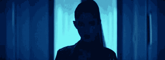a woman is standing in front of a window with a blue light behind her