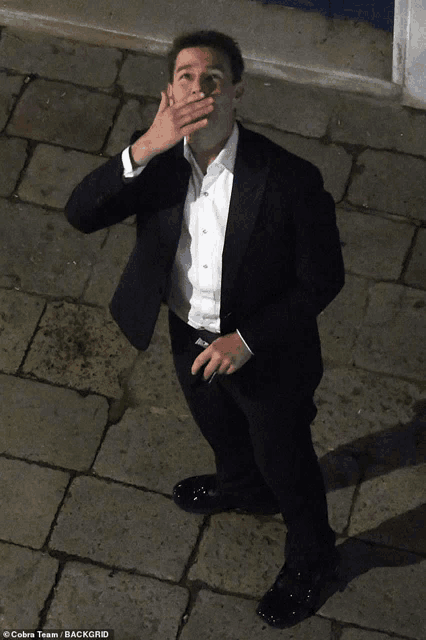 a man covering his mouth with his hand while wearing a black suit