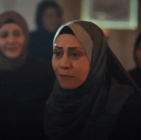 a woman wearing a hijab is making a funny face while standing in a crowd of people .