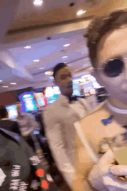 a man wearing sunglasses and a choker is standing next to another man in a casino .