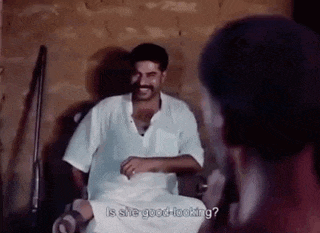 a man in a white shirt is talking to another man in a dark room .