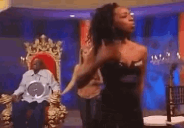a woman in a black dress is dancing in front of a man in a throne .