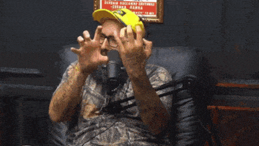 a man in a camo shirt is sitting in front of a microphone and making a funny face
