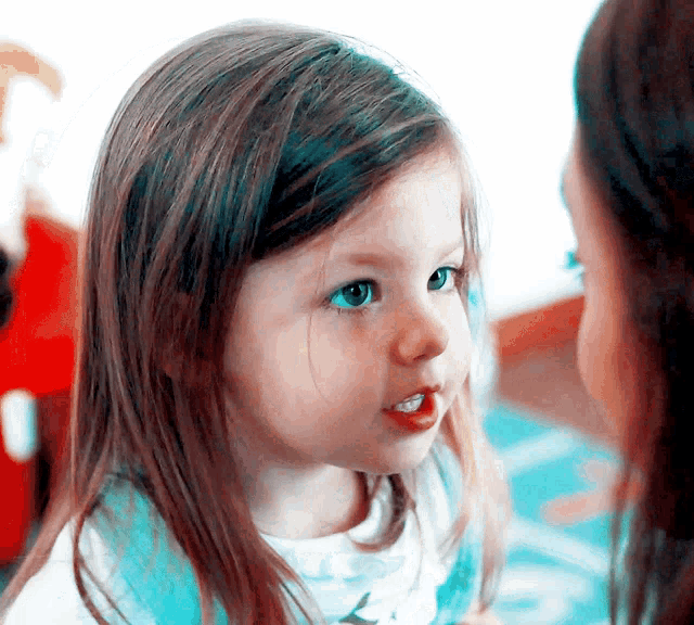 a little girl with long brown hair and blue eyes looks at her mother