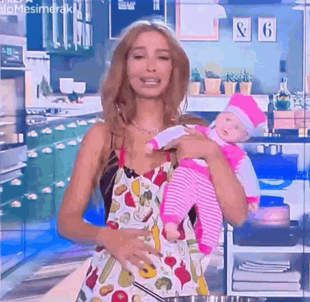 a woman in an apron is holding a baby doll in her arms in a kitchen .