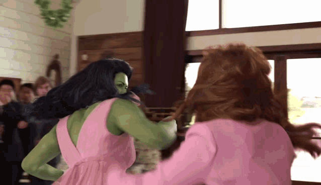a woman in a pink dress is standing next to a woman in a green costume