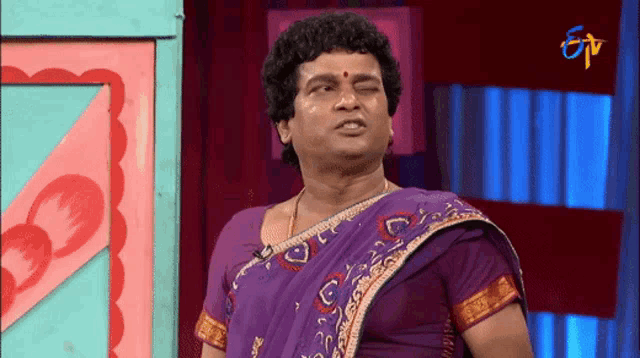 a man wearing a purple saree is standing in front of a colorful wall