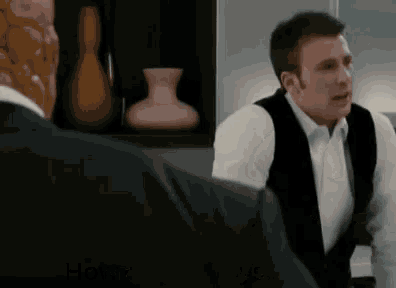 a man in a suit and white shirt is talking to another man in a kitchen .