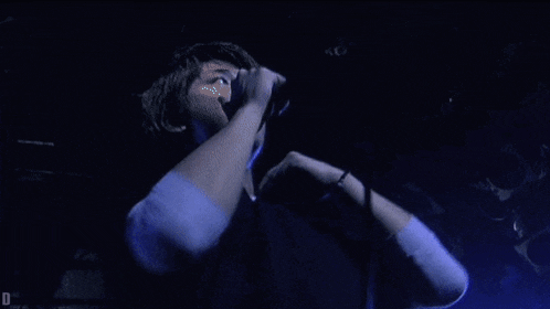 a man singing into a microphone in a dark room with the letter d on the bottom