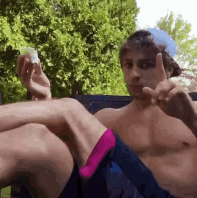 a shirtless man is sitting on a bench and making a peace sign with his fingers .