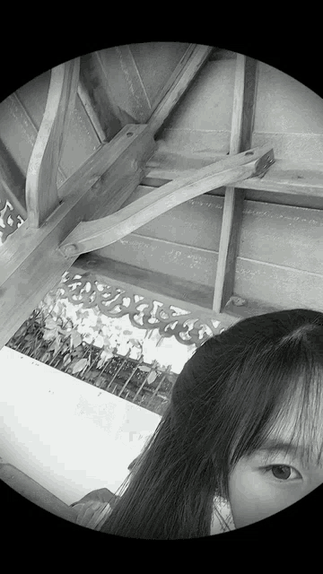 a black and white photo of a woman 's face with a wooden roof in the background