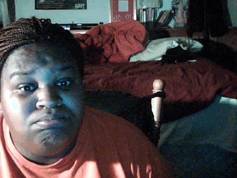 a woman in an orange shirt is sitting in front of a bed with a red blanket