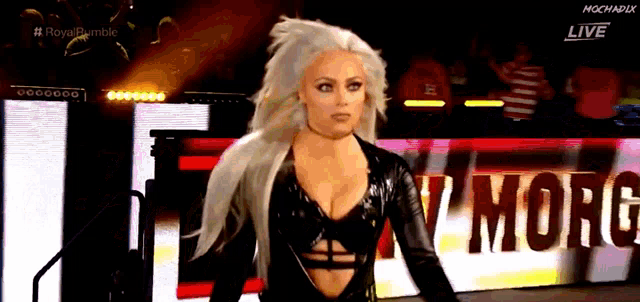 a woman in a black leather outfit is standing in front of a sign that says royal rumble live .