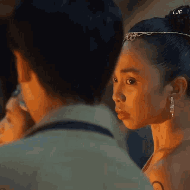 a woman wearing a tiara and earrings is looking at a man