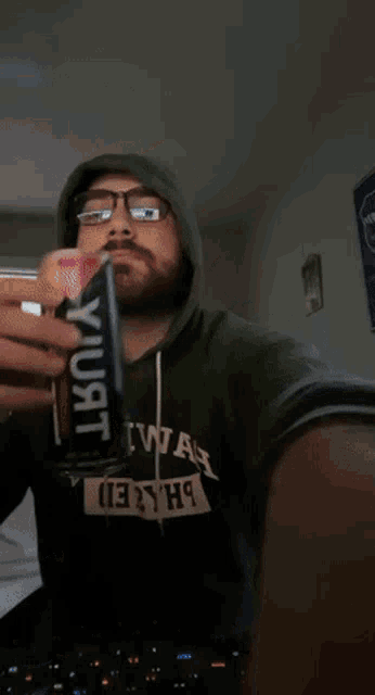 a man wearing a green hoodie that says 2hiwah on it is drinking from a can