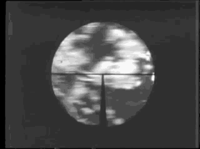 a black and white photo of a sniper scope with a blurred background