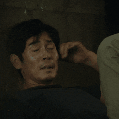 a man in a black shirt is leaning against a wall and looking down