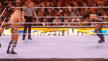 two women are wrestling in a wrestling ring with a referee standing between them .