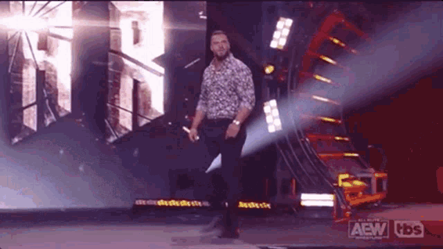 a man is standing on a stage holding a microphone in front of a large sign that says aew .