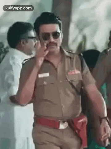 a man in a police uniform and sunglasses is standing in front of a crowd of people .