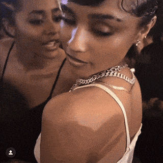 two women are standing next to each other in a dark room and one has a tattoo on her arm .